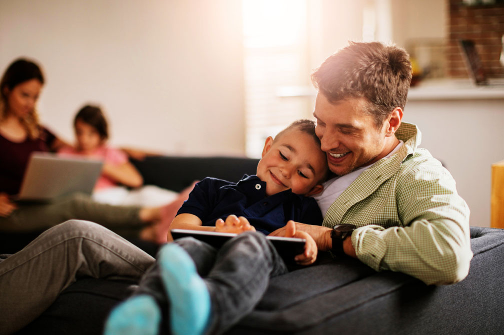 Father and son playing on iPad on sofa